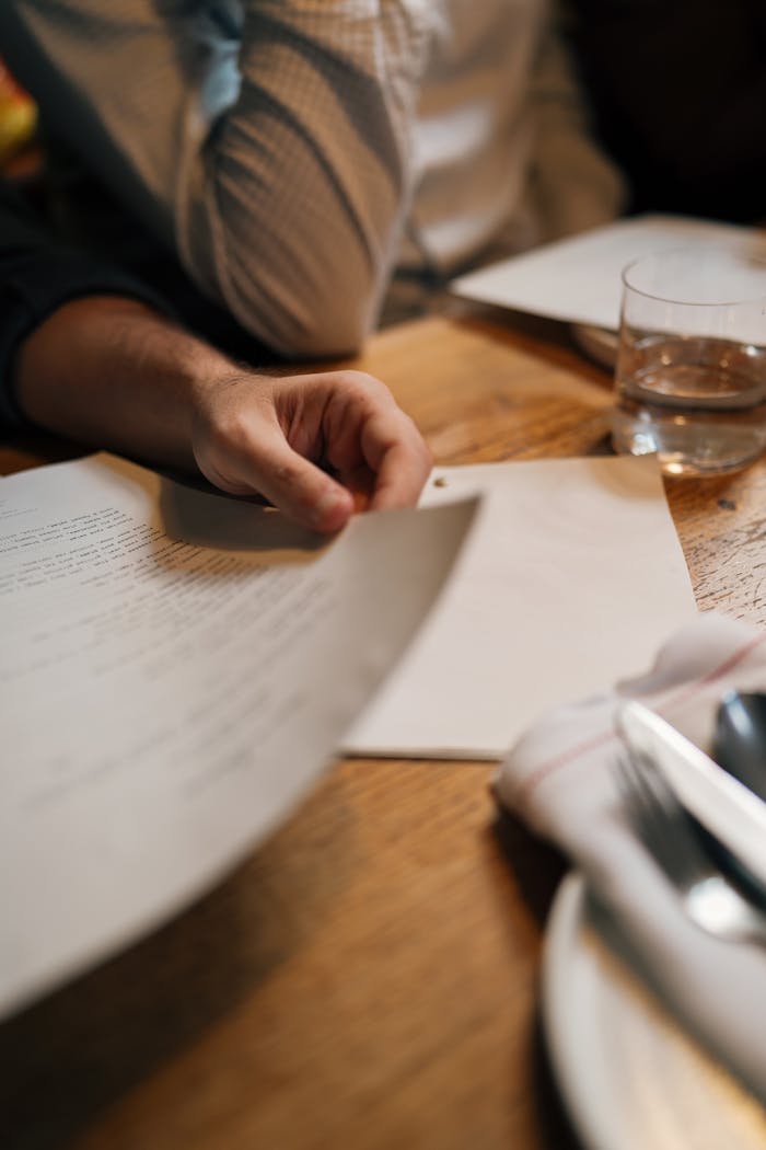 Close-up of a person reading a document at a wooden table with a glass of water.