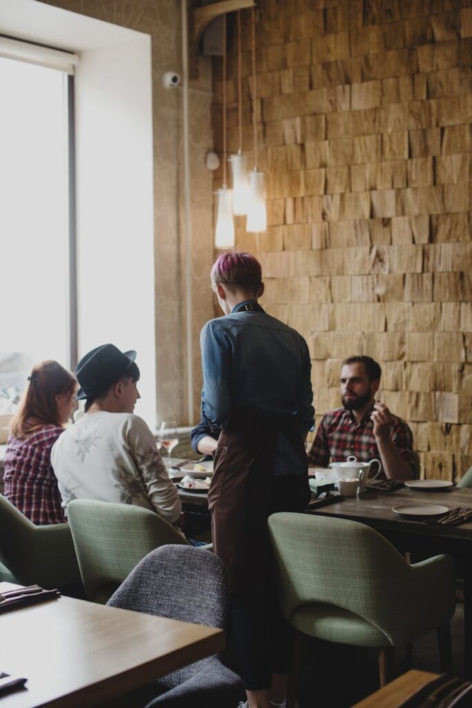 Anonymous male waiter wearing casual clothes standing near table with clients while listening attentively and accepting order
