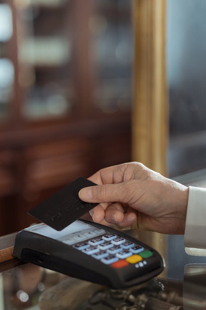 Close-up shot of a hand holding a credit card over a payment terminal in a store.